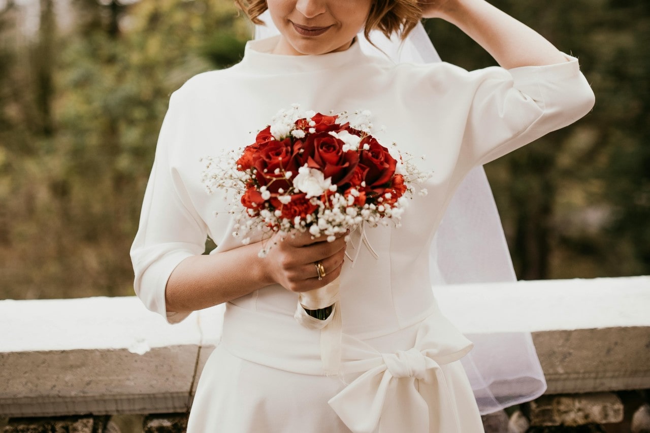 a woman in a wedding gown holding a bouquet of roses and wearing yellow gold wedding rings