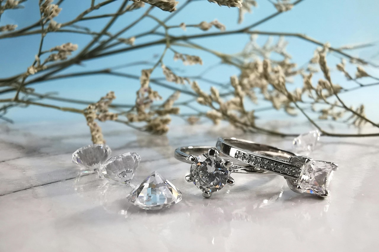 loose diamonds and diamond rings on a marble surface next to grass