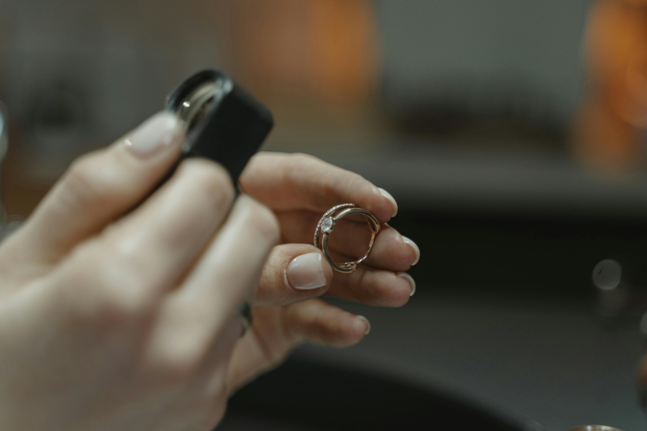 a pair of hands holding a jeweler’s loupe and examining a diamond ring