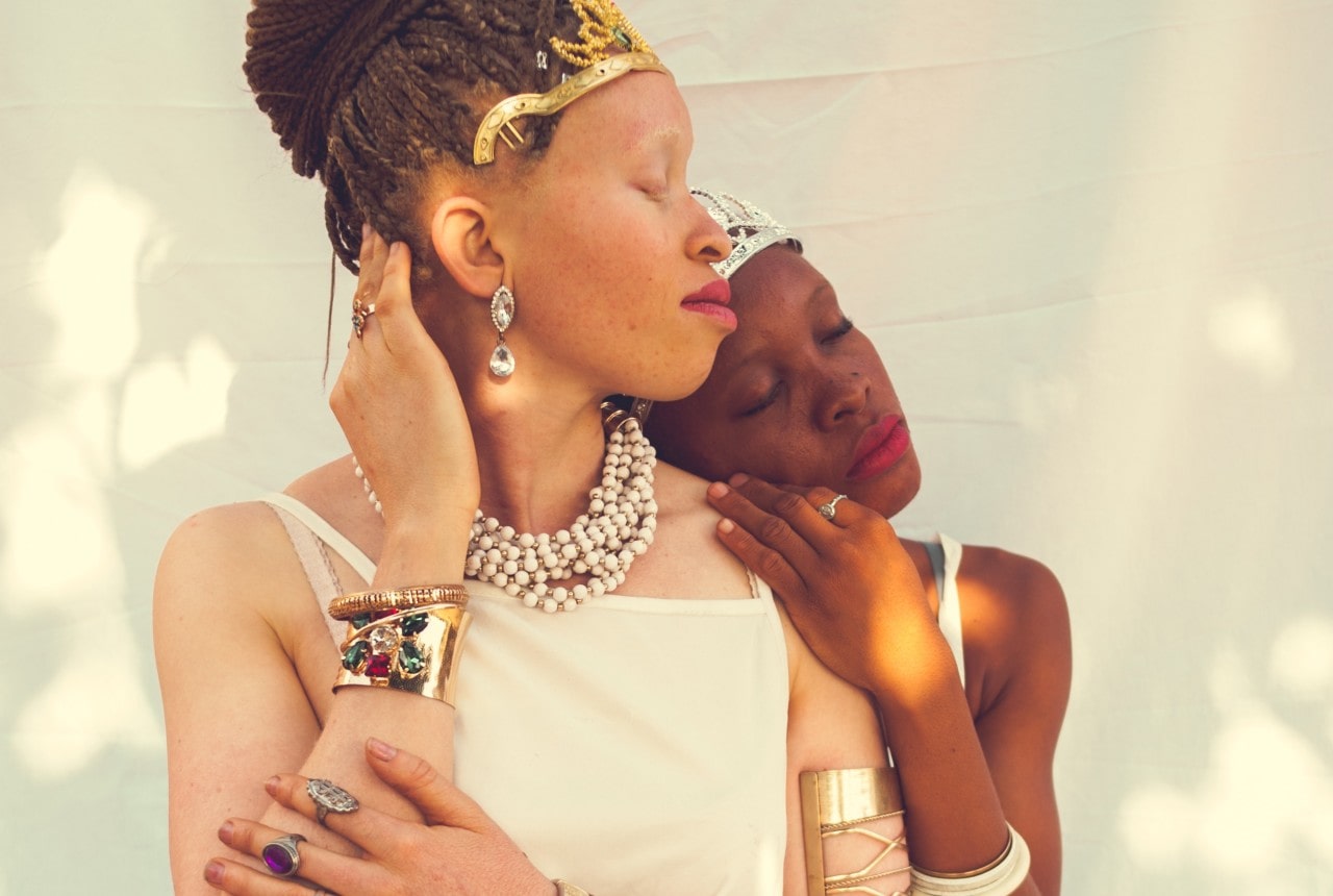 A bride and her maid of honor embracing, both adorned in opulent jewelry.