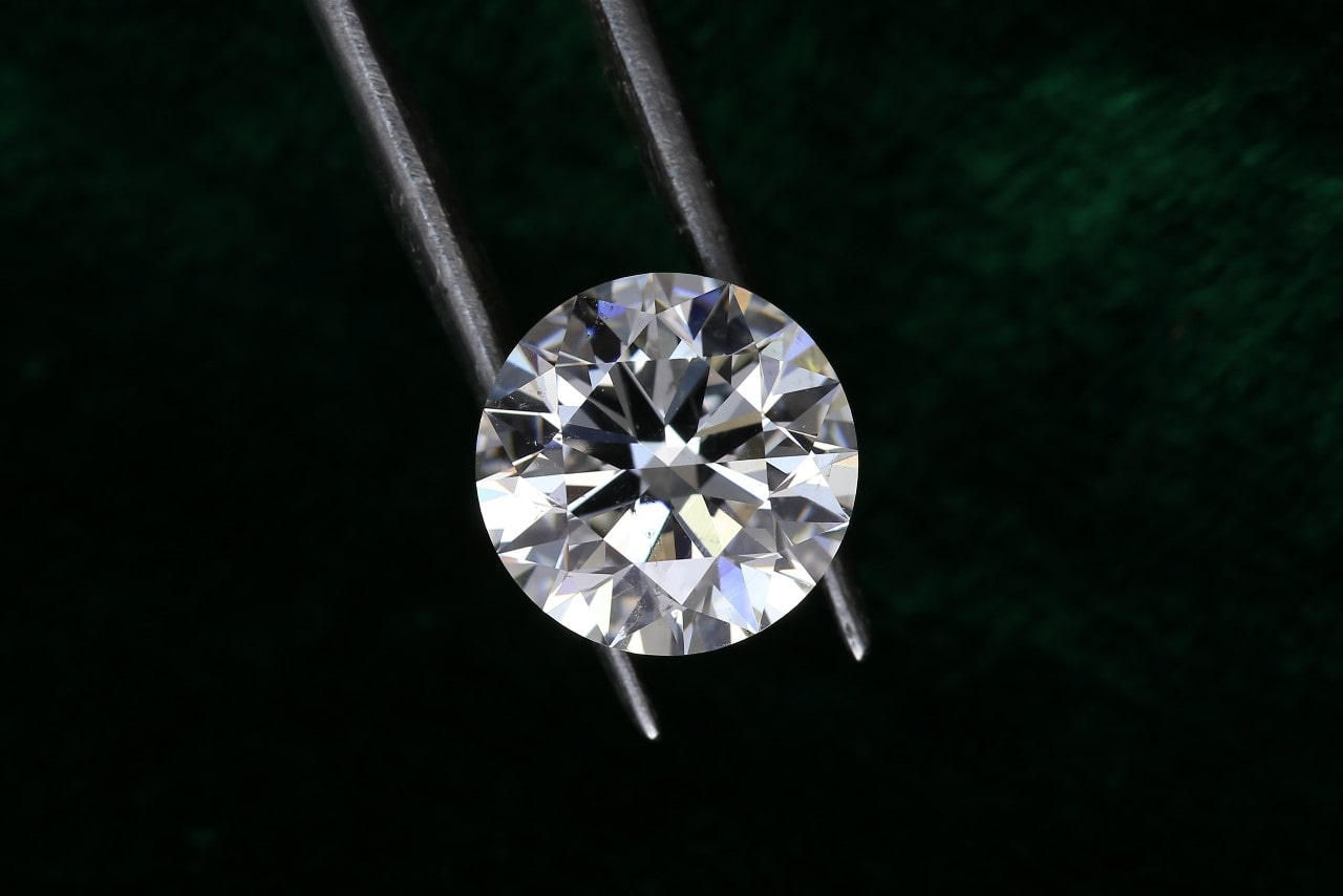 close up image of a round cut diamond help by silver tweezers against a black background