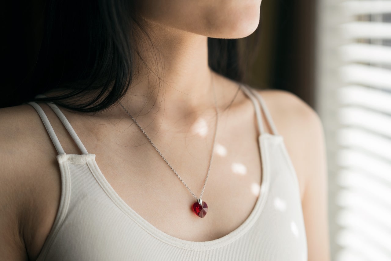 a woman looking out a window wearing a heart shaped ruby necklace