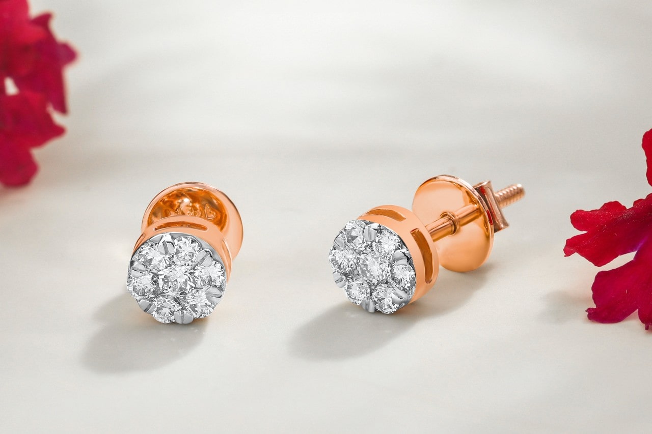 a pair of rose gold diamond stud earrings on a white surface surrounded by red flowers