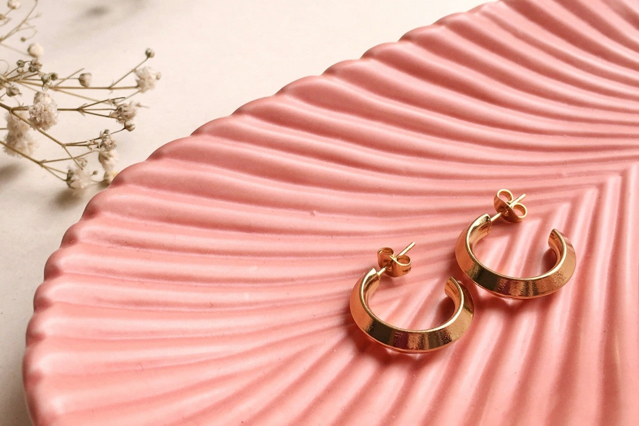 a pair of yellow gold huggie earrings on a pink, grooved dish