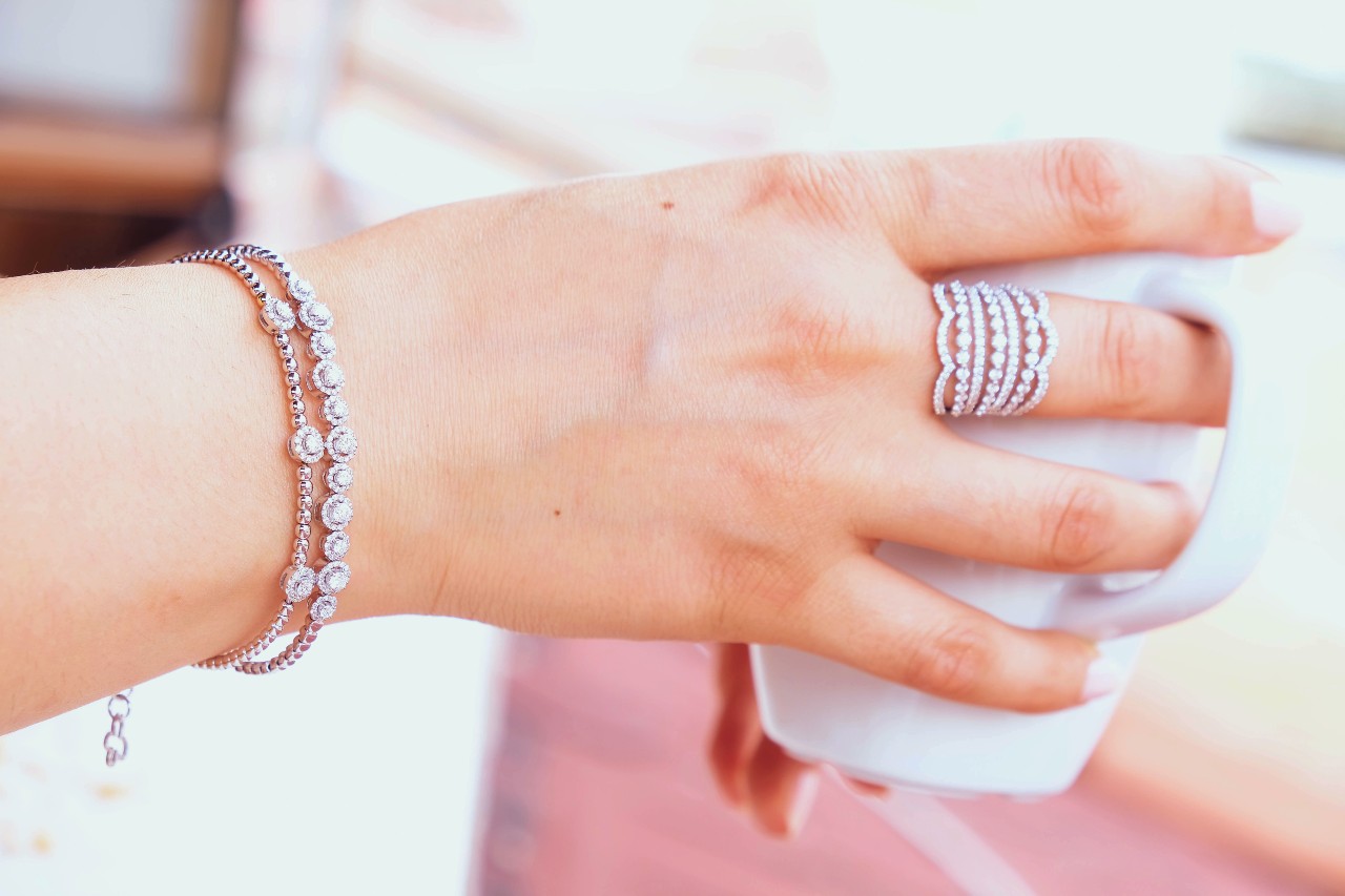 A close up of a woman's hand wearing white gold diamond bracelets and stackable diamond rings. A close up of a woman's hand wearing white gold diamond bracelets and stackable diamond rings.