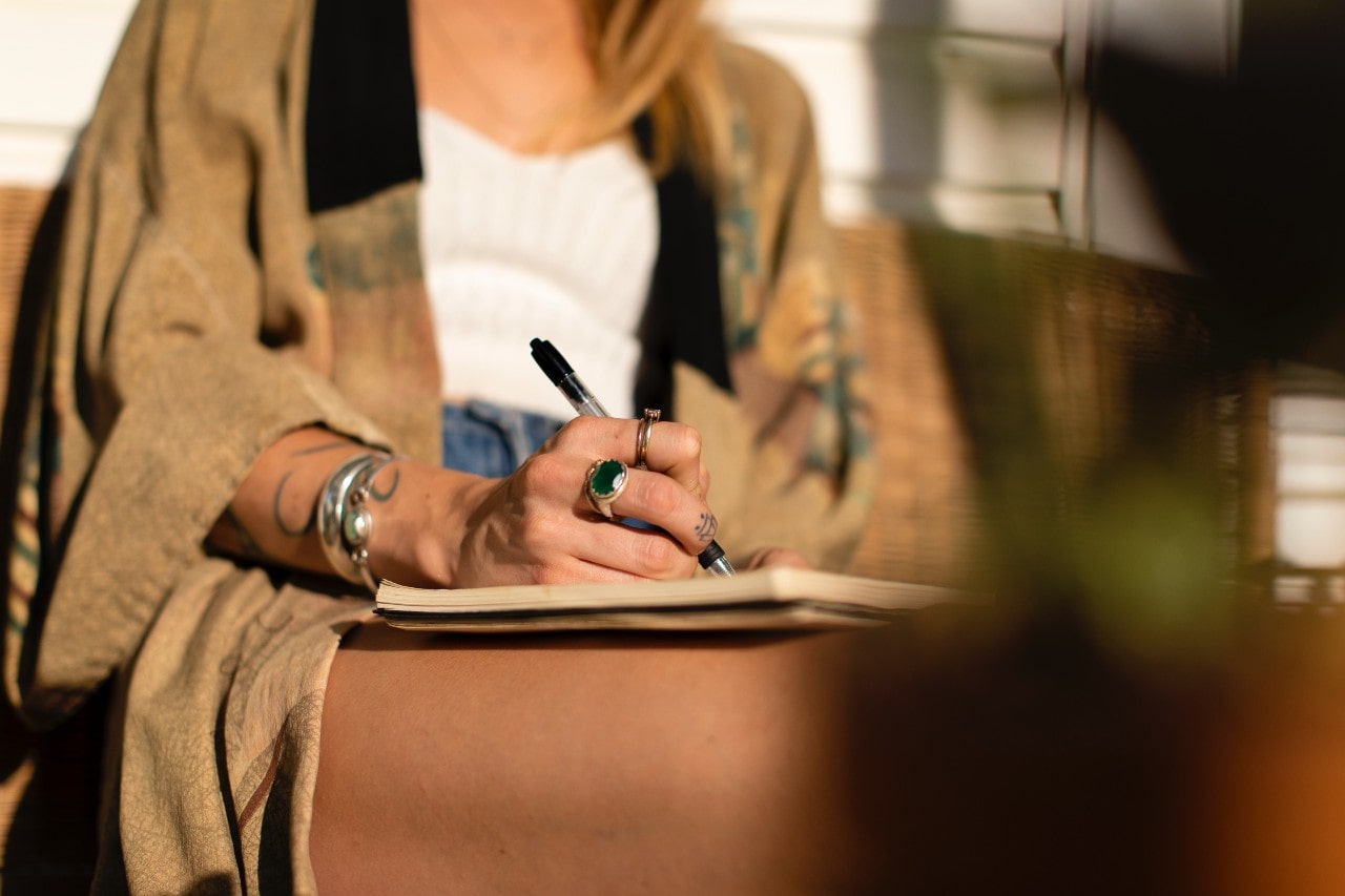 A woman sitting outside writing in a journal wears rings.