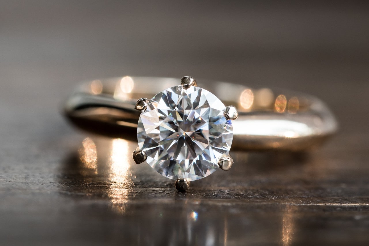 An elegant round cut solitaire ring displayed on a wooden tabletop.