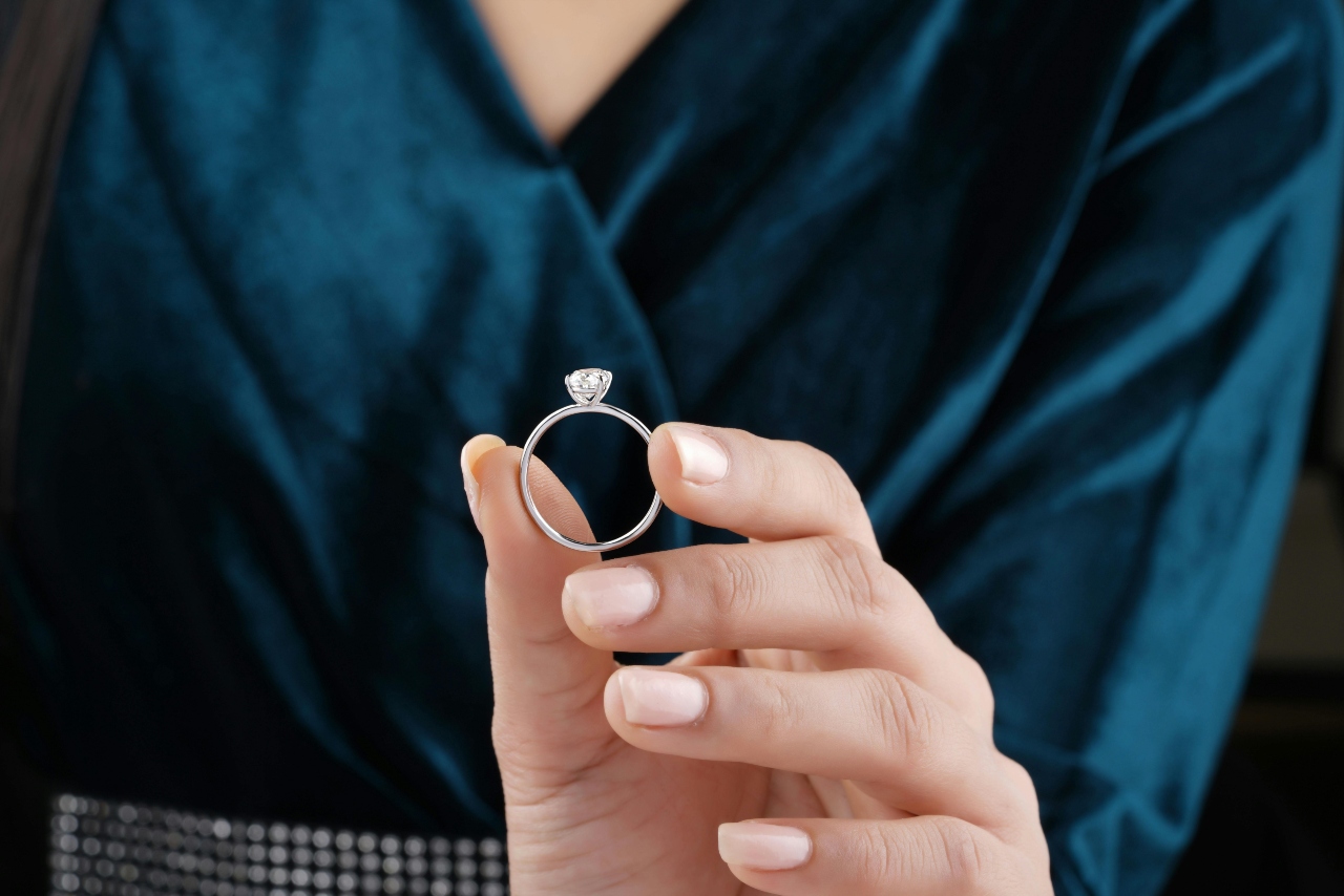 A close-up of a person holding a solitaire engagement ring in front of them.