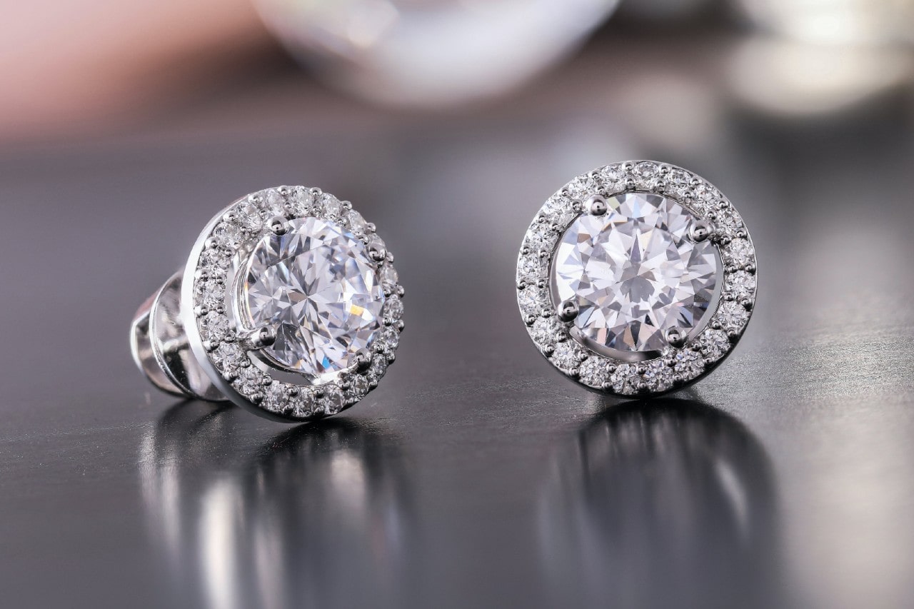 a pair of diamond halo stud earrings on a reflective metal surface