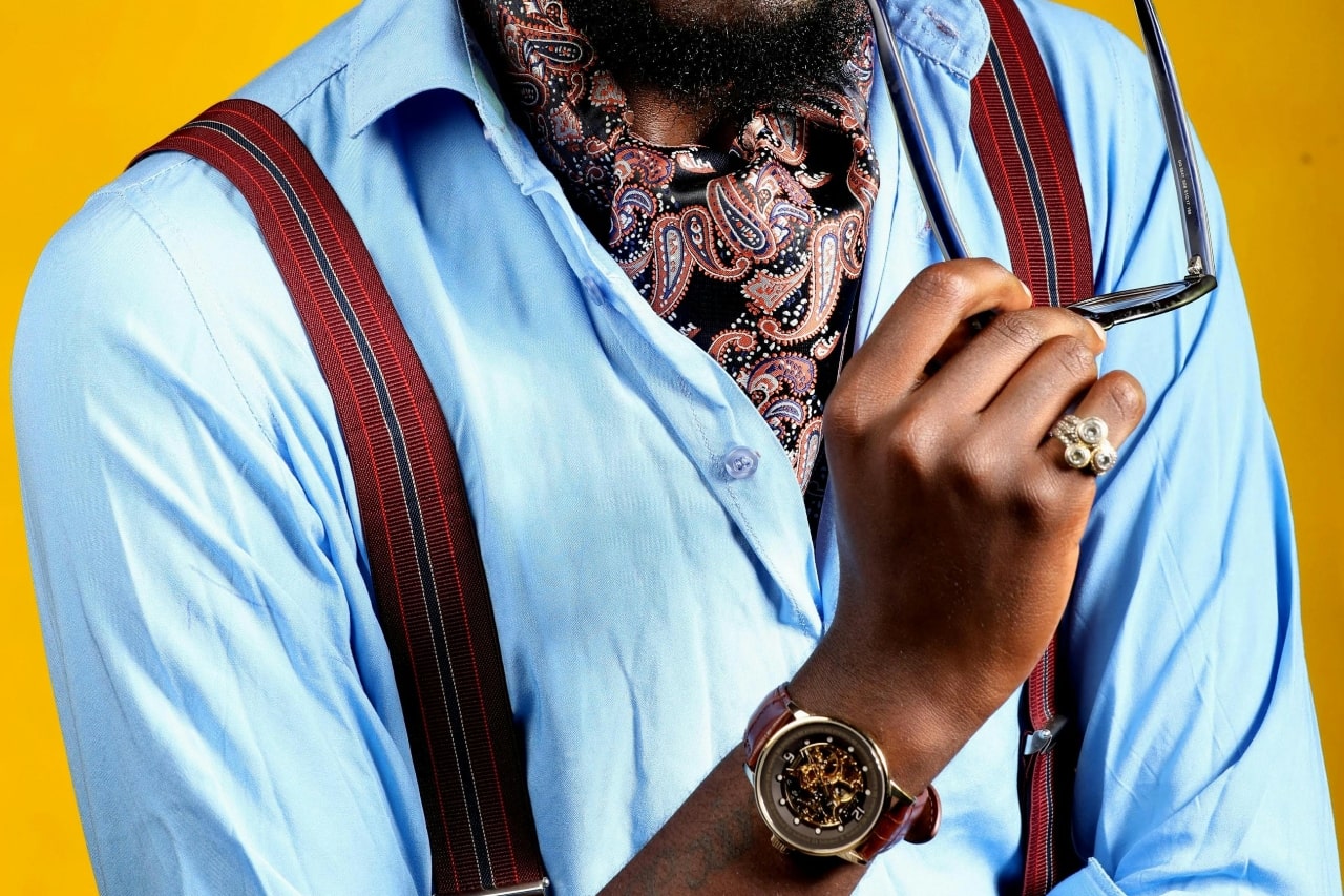 a man in a blue shirt lifting his glasses and wearing a skeleton dial watch