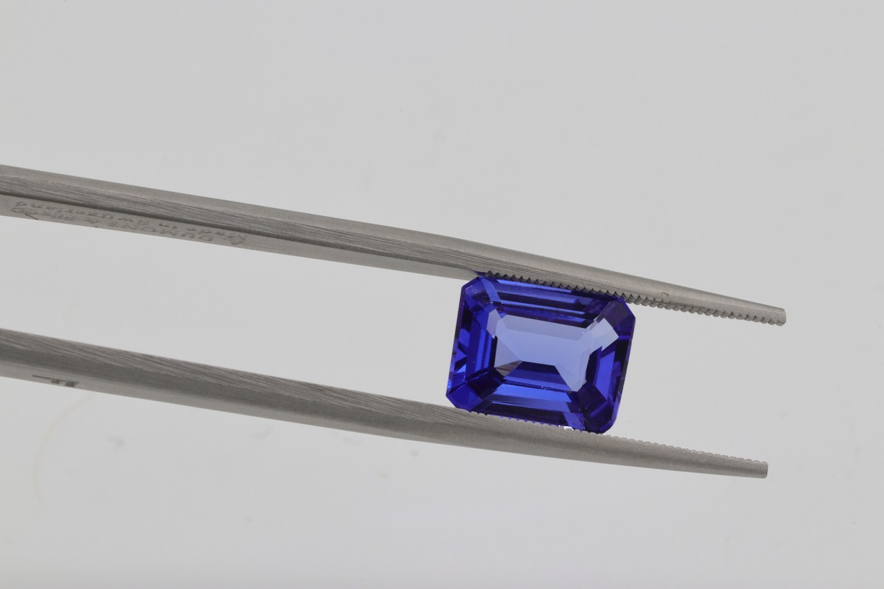 A close-up of a stunning sapphire held between the prongs of jeweler’s tweezers.