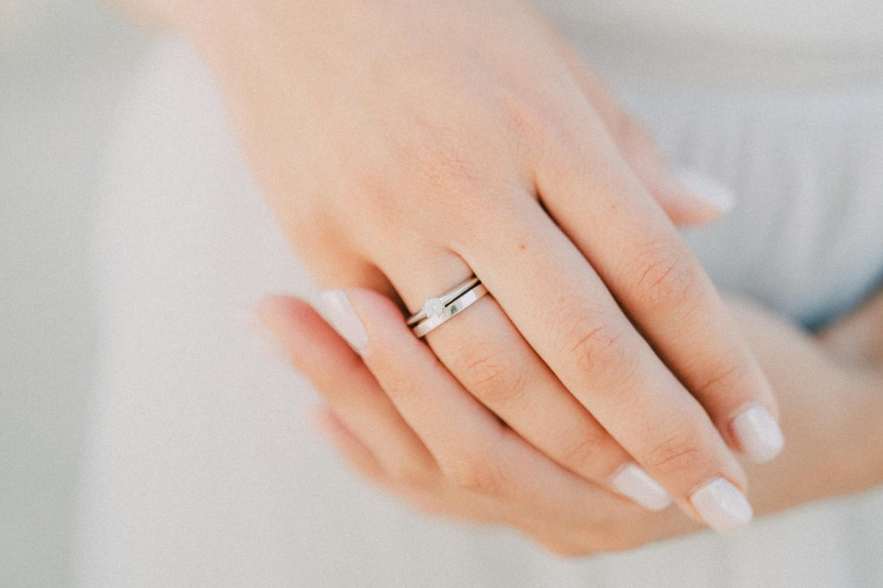 A bride’s hands, one of which is adorned with a simple engagement ring and wedding band.