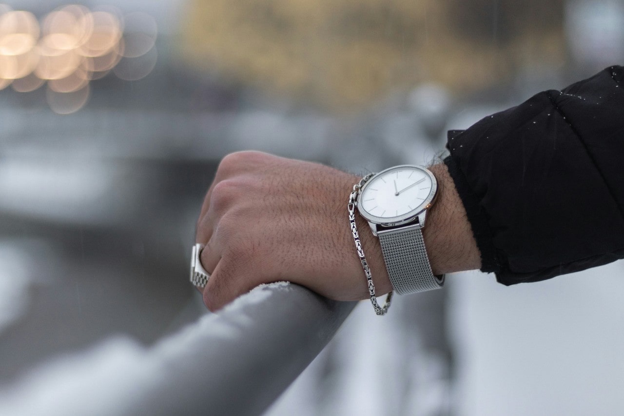 a person’s hand resting on a metal rail and wearing a silver watch