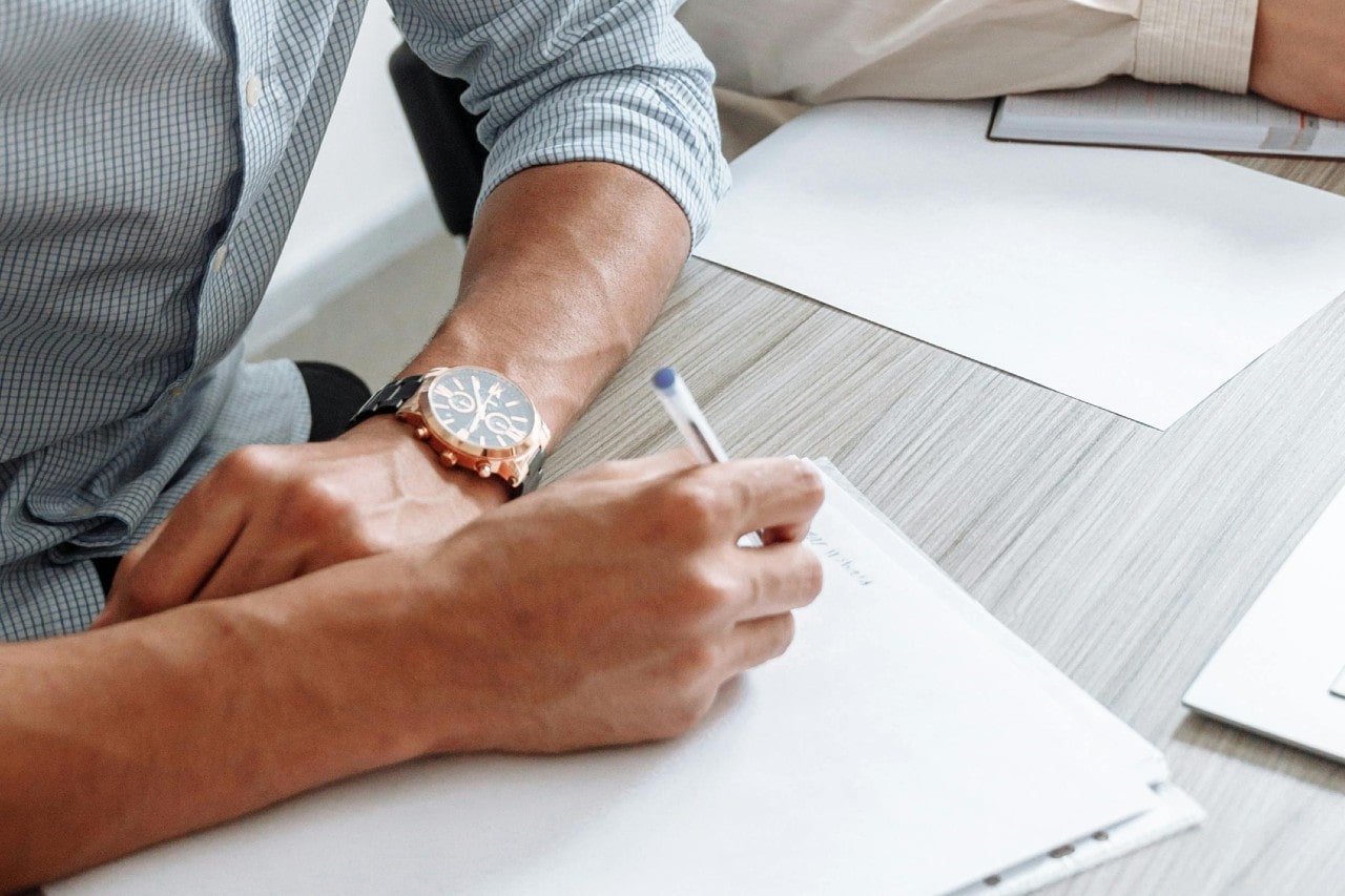 a business person writing on a pad and wearing a black and rose gold watch